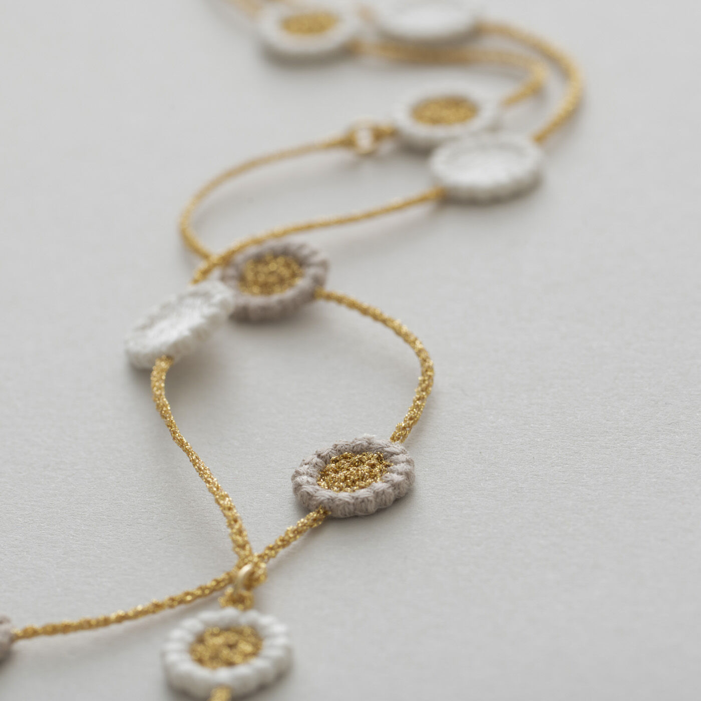 ＆Stories|群馬の刺繍工房が作った　糸の宝石のレースフラワーネックレス〈ゴールド色〉|糸の組み合わせによって表情が異なる3種類の花がリズムよく連なり、シンプルながら洗練された雰囲気を醸します。